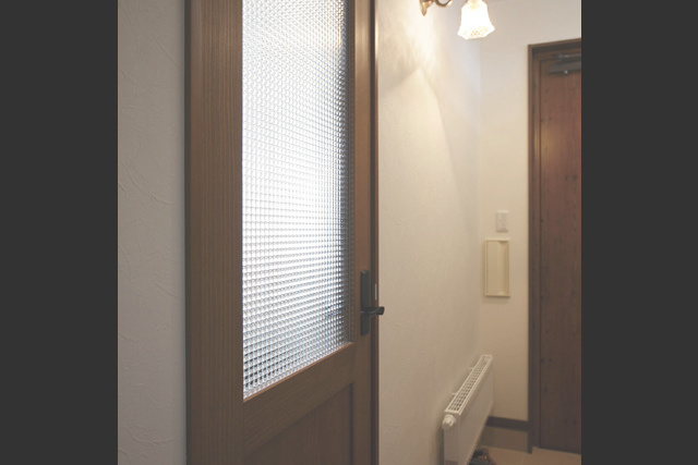 リビングドア： チェッカーガラスのリビングドアと ブラケット照明がアンティークな雰囲気を 醸すリビングの入口。